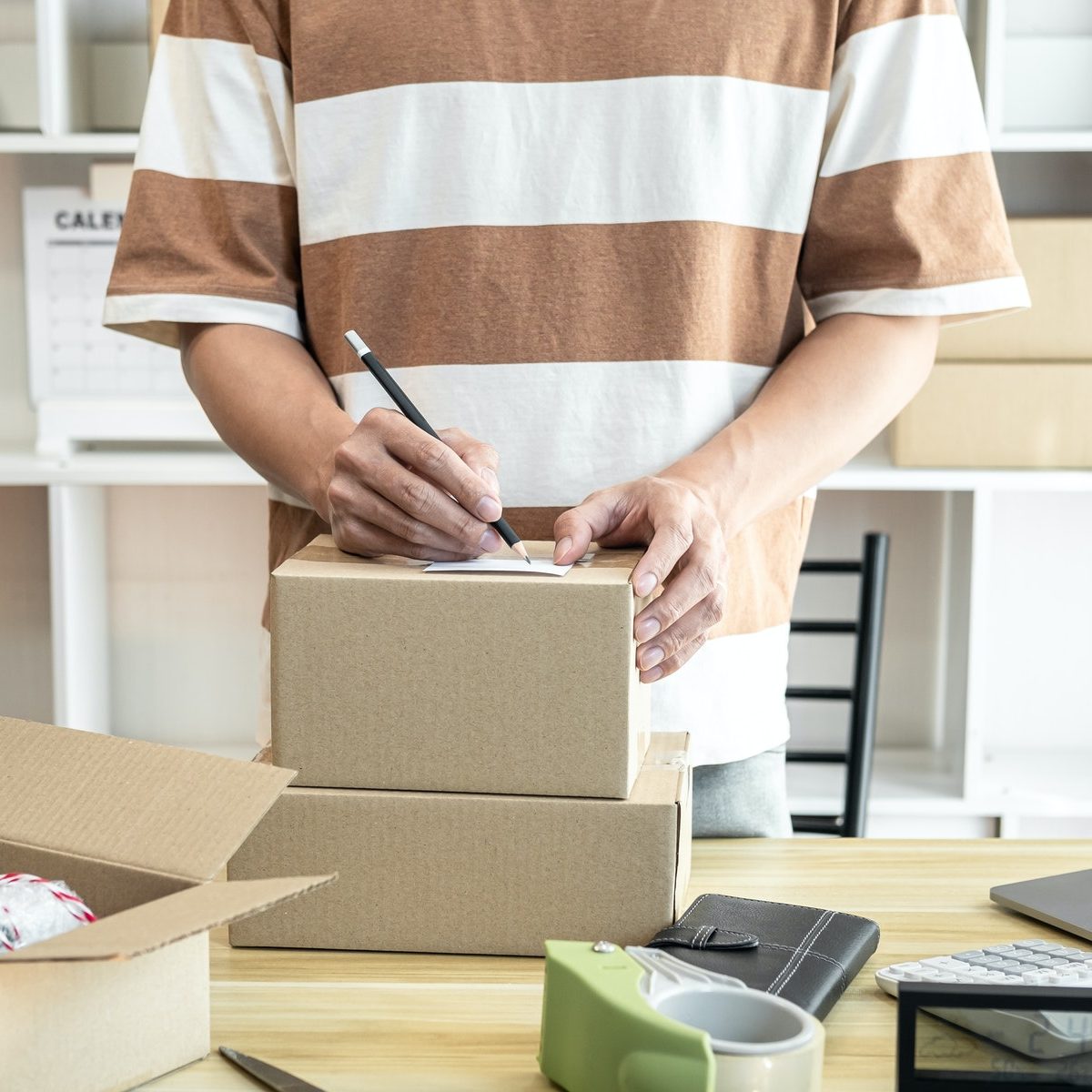 Male entrepreneur is writing address on cardboard boxes for prep